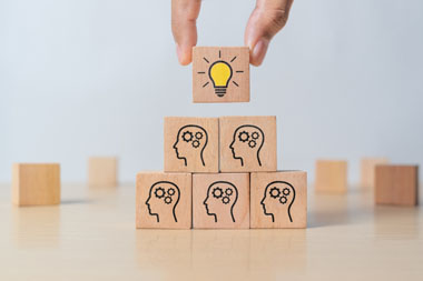 Piramide de caixinhas de madeira e na caixa mais acima o desneho de uma lampada simbolizando uma idéia concluida